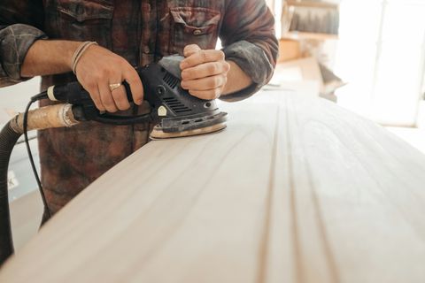 Hände schleifen eine Holzplatte mit dem Exzenterschleifer