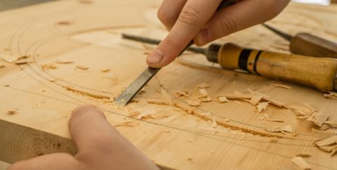 Hand führt einen Stechbeitel durch helles Holz, Späne liegen daneben