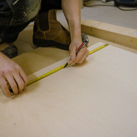 Hände messen mit einem Maßband und markieren mit Bleistift auf einer Holzplatte